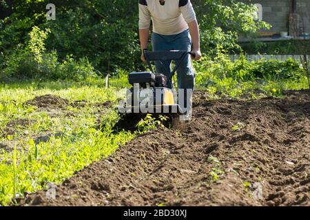Vue perspective de l'homme labourage le sol du jardin par cultivateur à moteur Banque D'Images