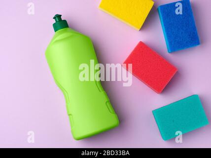 cuisine multicolore éponges rectangulaires pour lave-vaisselle et bouteille verte en plastique avec détergent, fond violet Banque D'Images