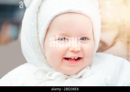 Portrait de petite fille caucasienne souriante à l'extérieur. Enfant tout-petit dans des vêtements chauds blancs marchant à l'extérieur. Rire drôle jeune enfant avec les yeux bleus Banque D'Images