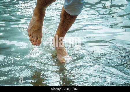 Barefoot man legs in cold mountain lake water Banque D'Images