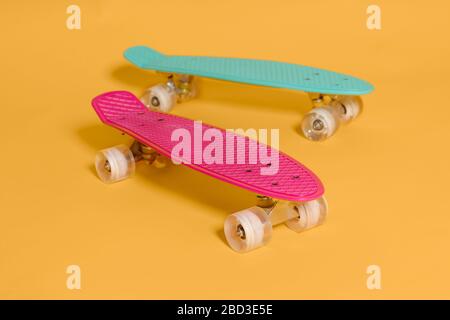 Deux penny skateboard rose et vert isolé sur fond jaune. Banque D'Images