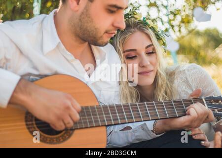 Un couple charmant passe du temps libre ensemble, date, bénéficie d'une atmosphère paisible en plein air dans les prairies. Le gars romantique joue de la guitare et chante des chansons à son Banque D'Images