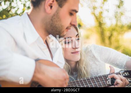 Un couple charmant passe du temps libre ensemble, date, bénéficie d'une atmosphère paisible en plein air dans les prairies. Le gars romantique joue de la guitare et chante des chansons à son Banque D'Images