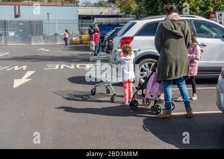 Les gens font la queue en ligne en observant les distances sociales en attendant d'entrer dans un supermarché pendant la pandémie de coronavirus. Banque D'Images