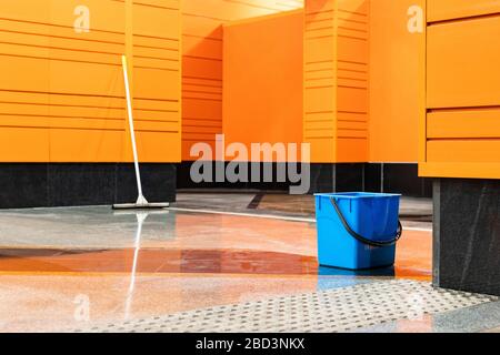 Désinfection des stations de métro pendant la pandémie de coronavirus. Seau en plastique bleu et balai à franges sur le fond d'une station vide avec une wa orange Banque D'Images