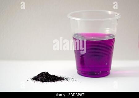 Poudre de permanganate de potassium sur fond blanc. Permanganate de potassium en poudre noire et verre en plastique à l'eau de rose. Une solution de potassium Banque D'Images