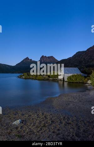 Des étoiles de l'heure bleue qui commencent à couvrir le légendaire lac Dove et le hangar de boatshed, menant aux deux pics de Cradle Mountain sur un ciel de nuit clair en Tasmanie. Banque D'Images