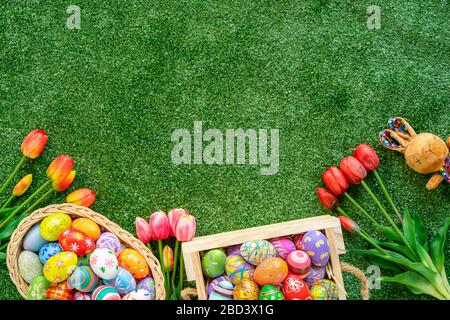 Mêlez des œufs de pâques peints colorés dans le panier avec des tulipes et une poupée de lapin sur fond vert d'herbe avec espace libre. Banque D'Images