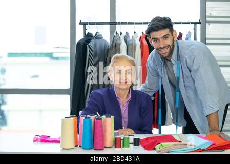 Ambiance matinale dans la boutique du tailleur. Le commerçant et les revues sur mesure travaillent quotidiennement sur la table pleine de tissus et de fils colorés. Un porte-vêtements Banque D'Images