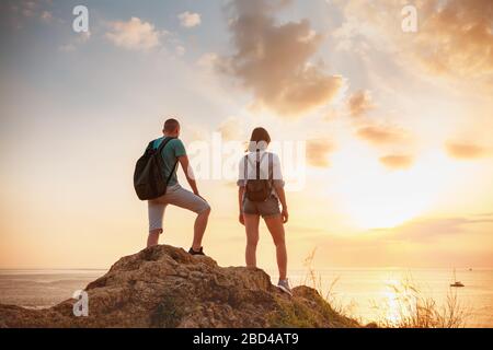 Deux jeunes randonneurs, hommes et femmes, se tiennent sur un grand rocher et regardent le coucher du soleil mer et le ciel Banque D'Images