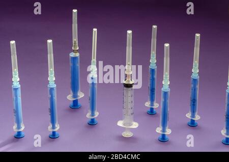 Groupe de seringues utilisées sur un fond lilas. Neuf seringues différentes sont disposées à la verticale. 8 bleu et un transparent. Prise de vue au niveau des yeux. Mise au point sélective. Banque D'Images