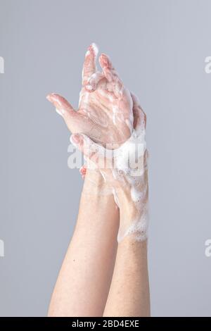 Les mains des blancs se lavant les unes les autres avec le savon de Marseille vert mousse isolé devant un fond gris avec des lumières et des ombres structurantes Banque D'Images