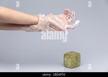 Les mains des blancs se lavant les unes les autres avec le savon de Marseille vert mousse isolé devant un fond gris avec des lumières et des ombres structurantes Banque D'Images