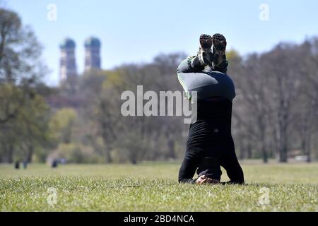 La vie publique en temps de pandémie de coronavirus le 5 avril 2020 dans le jardin anglais de Muenchen. Un homme de Bali fait du sport, fait des exercices. Les tours de la cathédrale notre-Dame sont visibles en arrière-plan. La météo printanière entraîne la population dans l'air frais, toujours avec la distance nécessaire en raison de l'infection par le virus corona. Restrictions de sortie, verrouillage de contact. | utilisation dans le monde entier Banque D'Images