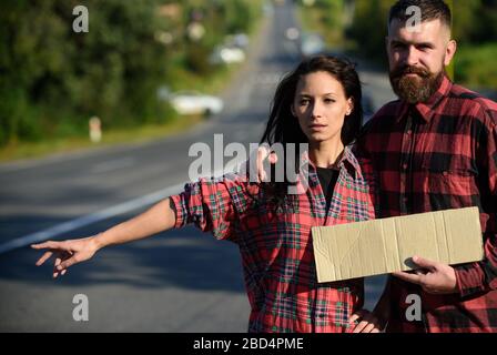 L'homme et la femme essaient d'arrêter la voiture avec un panneau en carton et un geste. Concept d'aventure et de randonnée. Couple avec des visages fatigués Voyage en arrêt automatique. Couple amoureux voyager par itchranking, espace de copie. Banque D'Images