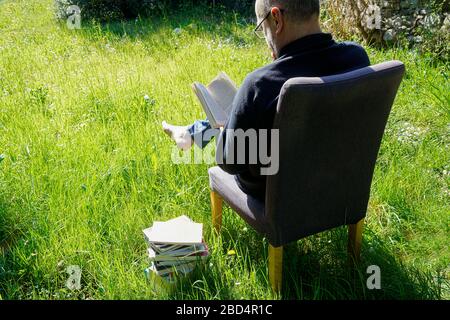 un homme lit un livre dans la pelouse du jardin pendant une quarantaine de coronavirus Banque D'Images