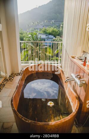 Baignoire en bois brun pleine d'eau sur le balcon avec vue pittoresque sur les palmiers de jungle verte dans le village d'Ao Nang dans la province de Krabi, Thaïlande Banque D'Images