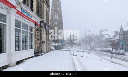 Paysage hivernal enneigé (neige, haute rue couverte de neige, église, boutiques et route dans le centre-ville pittoresque) - The Grove, Ilkley, Yorkshire, Angleterre, Royaume-Uni. Banque D'Images