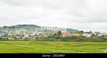 Paysage typique de Madagascar sur fond nuageux jour - rizières humides en premier plan, maisons sur de petites collines de la banlieue Antananarivo Banque D'Images