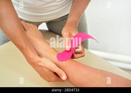 Jeune physiothérapeute appliquant du ruban de kinésiologie rose sur les pieds de la patiente, détails de la fermeture Banque D'Images