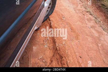 Conduire le véhicule 4 rm sur une route rouge poussiéreuse avec de grands trous, détail sur les pneus avec basse pression sur terrain accidenté. Les routes sont en mauvais état Banque D'Images