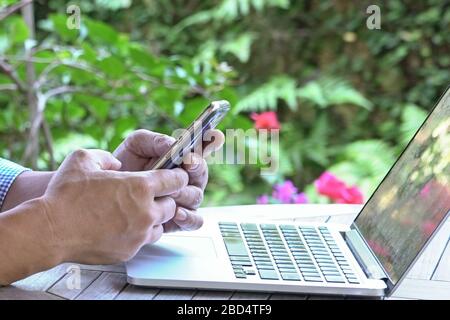 Vue détaillée de la messagerie des mains de l'homme avec son téléphone portable devant son ordinateur portable. Banque D'Images
