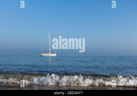 Bateau à voile ancré au large de la rive avec une vague de rupture au premier plan à Hengistbury Head, près de Christchurch, Dorset, Angleterre, Royaume-Uni Banque D'Images