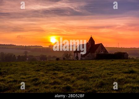 Coucher de soleil sur le parc national de South Downs à Idsworth avec l'église isolée de St Hubert dans un champ et un ciel bleu et orange spectaculaire Banque D'Images