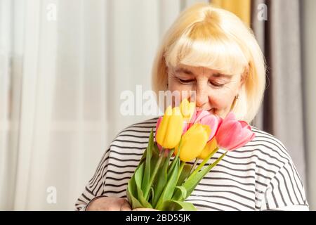 Adulte jolie femme blonde qui ronfle un bouquet de fleurs de tulipes sur fond gris. Bonne fête des mères. Banque D'Images