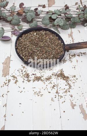 Une cuillère de basilic séché déborde sur une table en bois blanc Banque D'Images