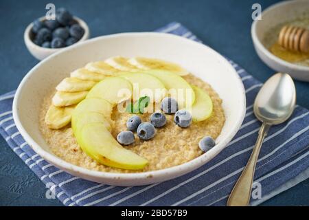 Flocons d'avoine avec bananes, bleuets, confiture, miel, serviette bleue sur fond de pierre bleue. Banque D'Images