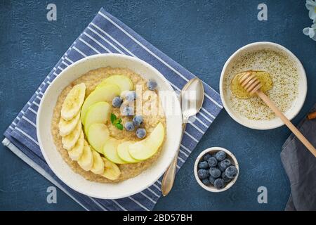 Flocons d'avoine avec bananes, bleuets, confiture, miel, serviette bleue sur fond de pierre bleue. Banque D'Images