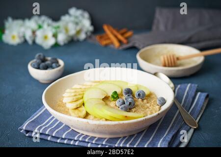 Flocons d'avoine avec bananes, bleuets, confiture, miel, serviette bleue sur fond de pierre bleue. Banque D'Images