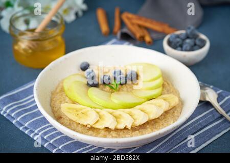 Flocons d'avoine avec bananes, bleuets, confiture, miel, serviette bleue sur fond de pierre bleue. Banque D'Images