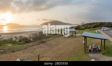 En regardant vers Cabbage Tree et les îles Boondelbah alors que le soleil réchauffe la plage de Bennetts à Hawks Nest sur la côte nord de la Nouvelle-Galles du Sud, en Australie Banque D'Images