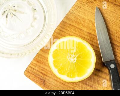 Un citron divisé en deux sur une planche à découper en bois avec un couteau de cuisine et un presse-citron en verre sur une nappe blanche Banque D'Images