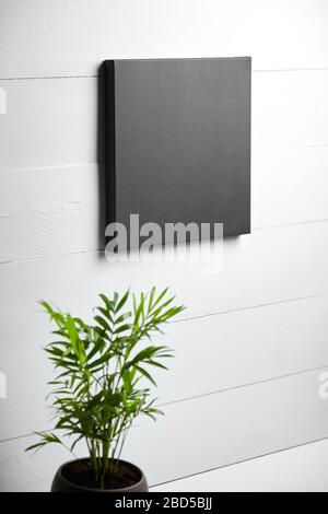 Une toile de coton noir et une plante verte sur fond de bois blanc. Toile propre étirée accrochée au mur. Maquette, vue latérale Banque D'Images