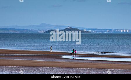 Portobello, Édimbourg, Écosse, Royaume-Uni. 7 avril 2020. Eeerily Plage tranquille avec un homme et une famille marchant, le long de la rive avec Inchkeith Island i n arrière-plan. Les résidents ayant pris en compte le programme de verrouillage britannique des coronavirus, il n'y avait que très peu de personnes. Banque D'Images