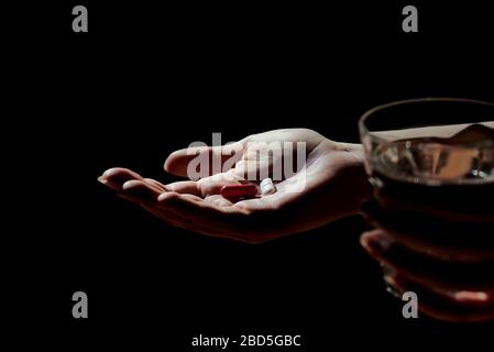 Vue rapprochée de la main d'une femme ou d'une fille tenant des comprimés de médicament, des comprimés et du verre d'eau. Photo de nuit avec contraste élevé, fond noir et spa Banque D'Images