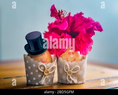 Joli couple d'œufs de Pâques avec des visages dessinés, décoré avec un chapeau et une fleur d'hibiscus dans des tasses à œufs. Concept créatif. Banque D'Images