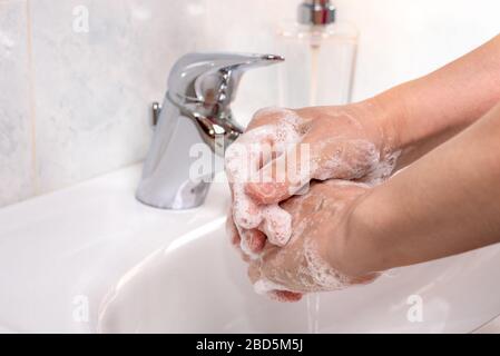 Femme utilisant du savon et de l'eau chaude pour se laver les mains sur un lavabo dans une salle de bains. Prévention de la pandémie de coronavirus. Banque D'Images