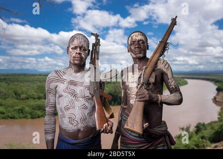 Affichant sa carabine et sa peinture corporelle au-dessus de la rivière Omo, une tribu Karo ou un membre d'un groupe ethnique, Tumi, Ethiopie. Banque D'Images