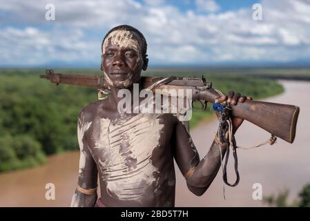 Affichant sa carabine et sa peinture corporelle au-dessus de la rivière Omo, une tribu Karo ou un membre d'un groupe ethnique, Tumi, Ethiopie. Banque D'Images