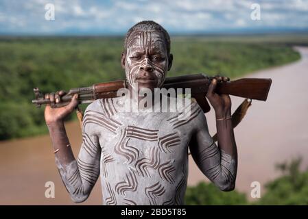 Affichant sa carabine et sa peinture corporelle au-dessus de la rivière Omo, une tribu Karo ou un membre d'un groupe ethnique, Tumi, Ethiopie. Banque D'Images