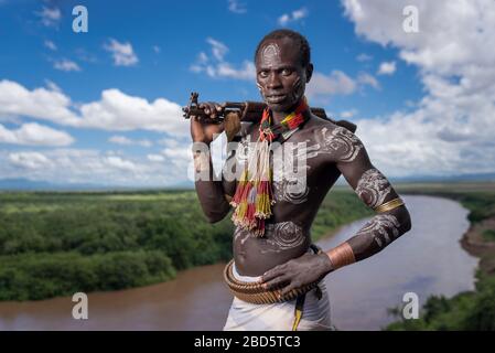 Affichant sa carabine et sa peinture corporelle au-dessus de la rivière Omo, une tribu Karo ou un membre d'un groupe ethnique, Tumi, Ethiopie. Banque D'Images