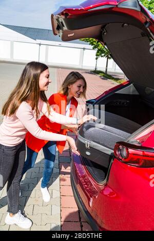 Les filles ont placé la valise de voyage dans le grand coffre de la voiture Banque D'Images