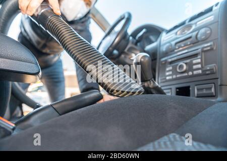 passer l'aspirateur à l'intérieur d'une voiture de tourisme à l'aide d'un aspirateur industriel. l'homme travaille dans un masque médical de protection. protection contre le coronavirus Banque D'Images