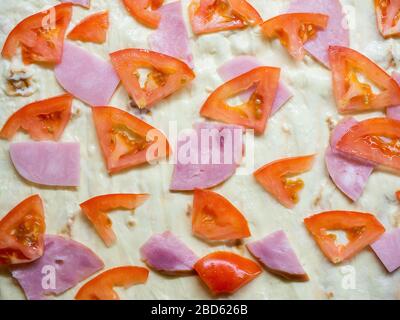 Des morceaux de jambon et de tomates sont soigneusement disposés sur une pâte fine graissée avec de la mayonnaise Banque D'Images