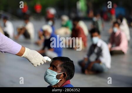 Delhi, Inde. 7 avril 2020. Un volontaire utilise un dispositif thermique sur un homme pour vérifier sa température en tant que travailleurs de salaire quotidien et sans-abri effectuent du yoga dans le complexe sportif Yamuna qui a été transformé en camp de fortune pour ceux qui ont été échoués à Delhi sans domicile pendant un verrouillage national dans le sillage du coronavirus pandémie. Le gouvernement indien a imposé un verrouillage national de 21 jours pour réduire au minimum la propagation de la maladie de Coronavirus (Covid-19). Crédit: SOPA Images Limited/Alay Live News Banque D'Images