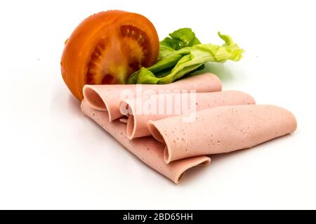 Tranche de jambon ou de saucisse de Paris sur fond blanc avec une demi-tomate et une feuille de salade Banque D'Images